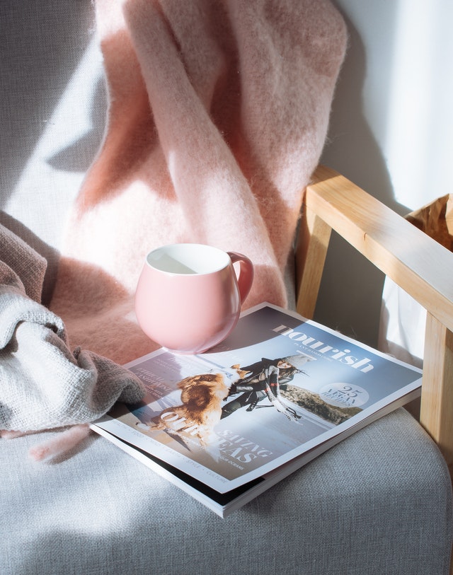 Steaming mug on chair with blanket and magazine