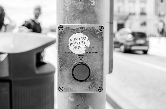 black and white image of button on pole with white sticker above and trash can in background