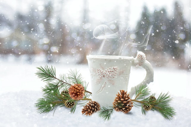 Steaming white mug in the snow surrounded by pine cones