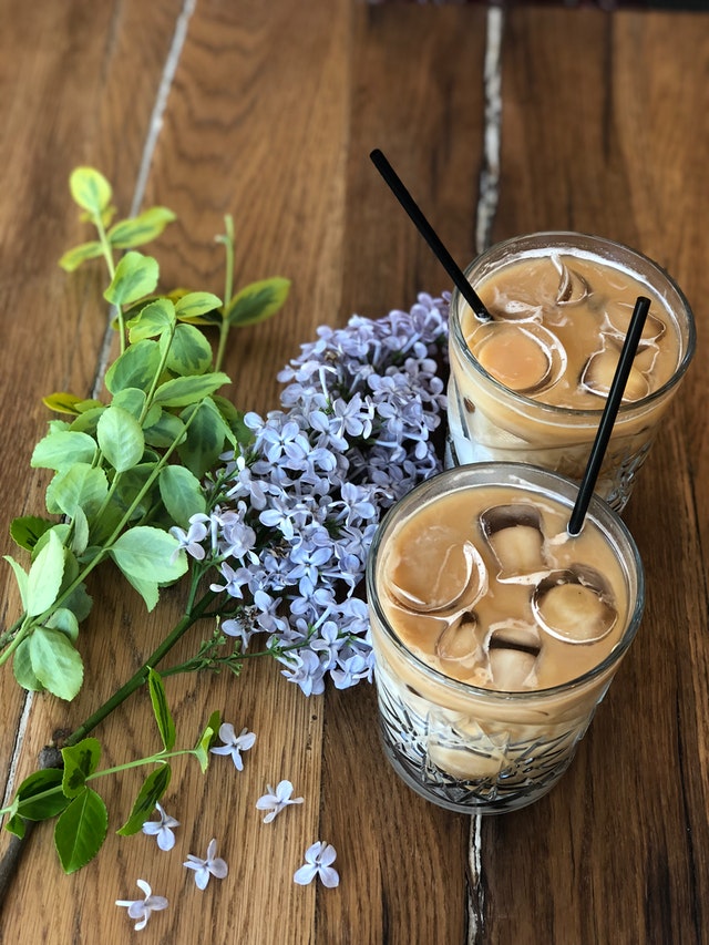 Two iced coffees on table next to lilac