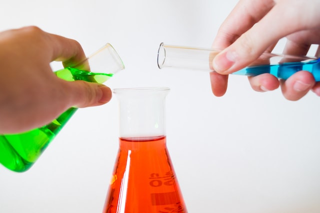Two flasks of colored liquid getting poured into one beaker